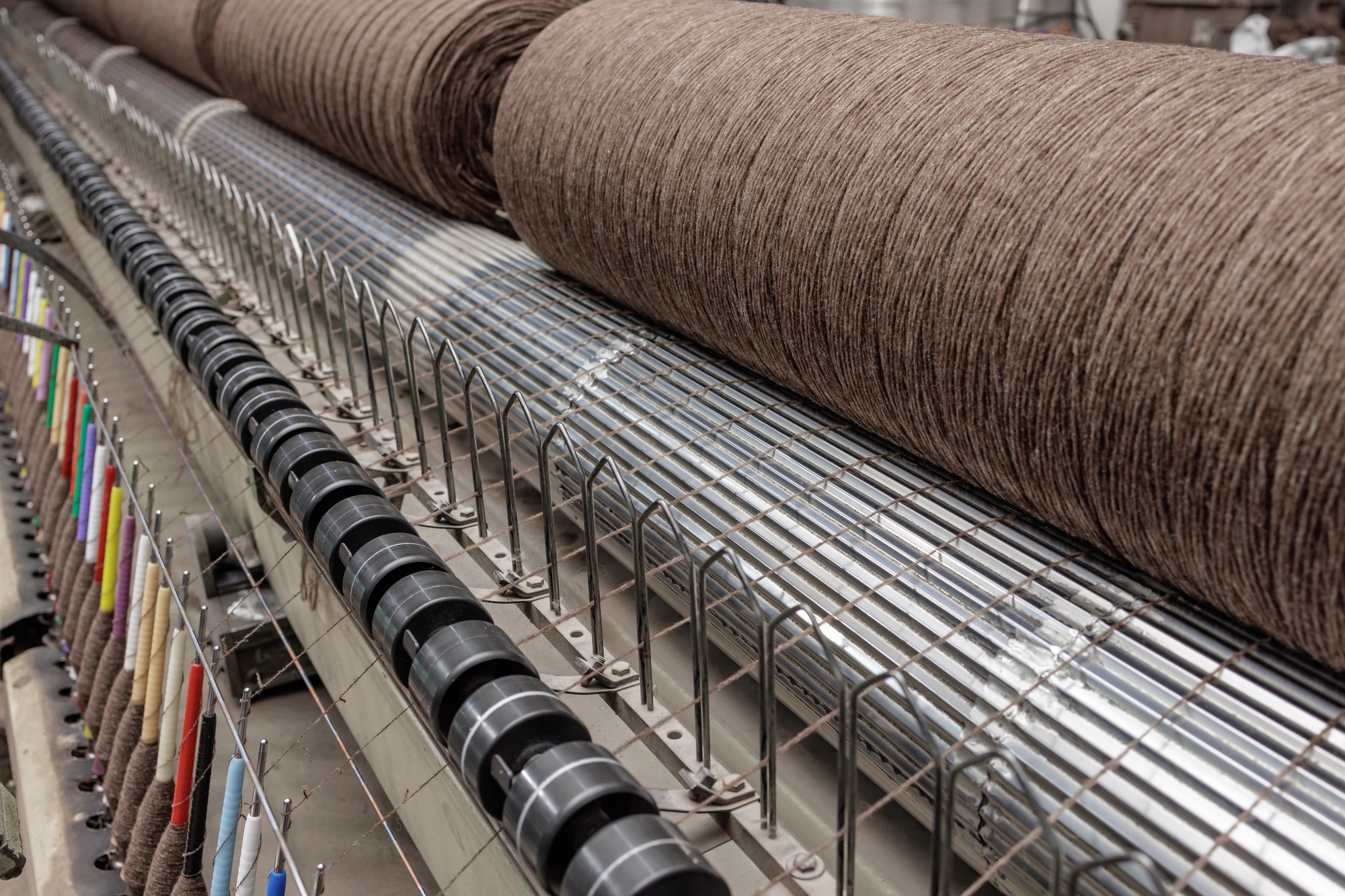Brown yarn on textile machine in factory, with colorful thread guides and rollers in production.